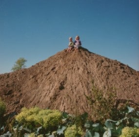 Maize and Eliza Diffley sitting on top of scrapped soil next to broccoli at the Gardens of Eagan during suburban development.